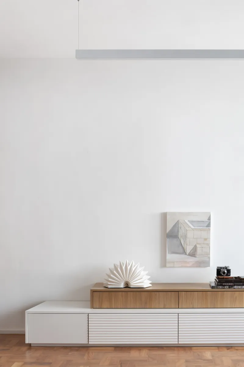 Low storage unit with timber and white panels beneath a white wall with pendant light