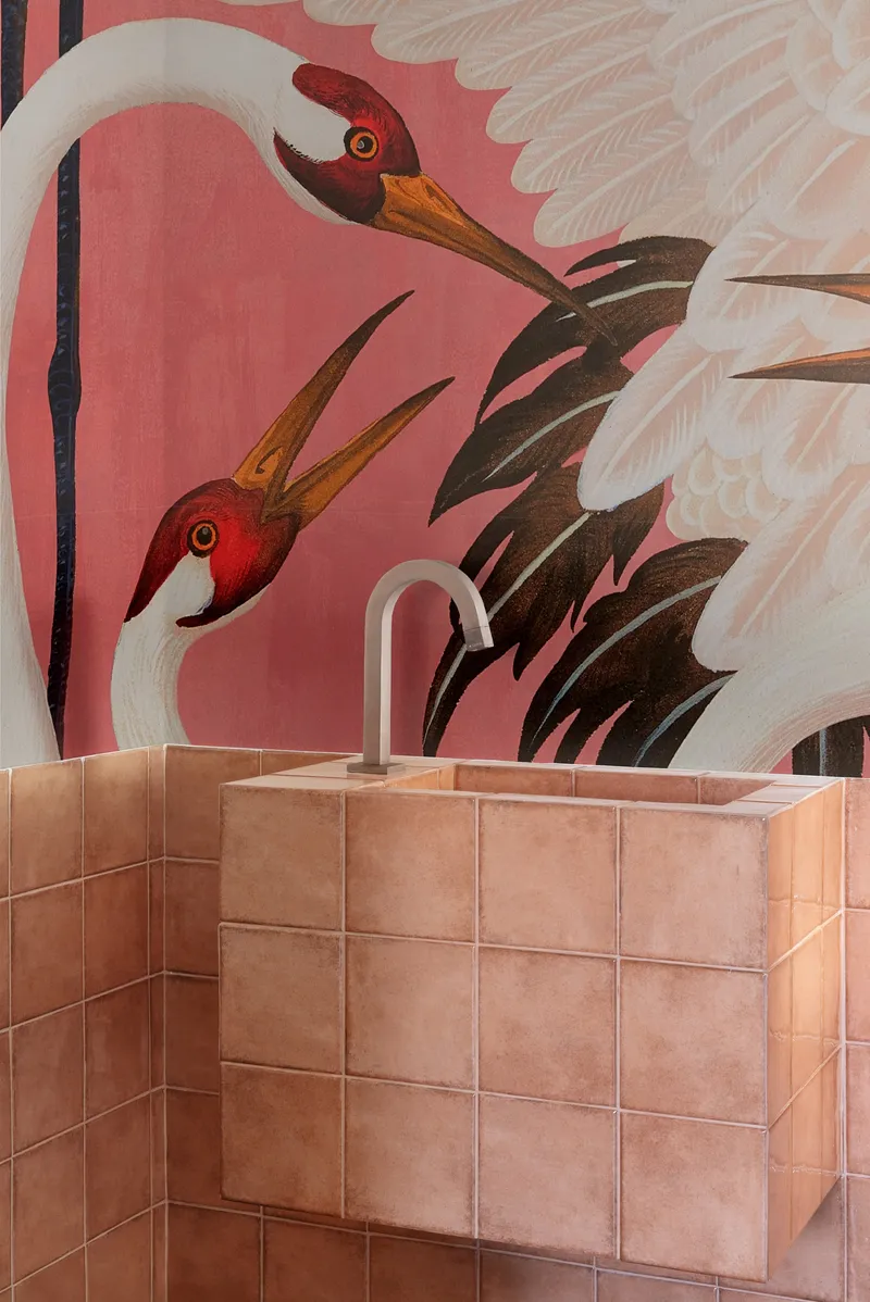 Tiled vanity basin with curved faucet against a pink mural of cranes and feathers