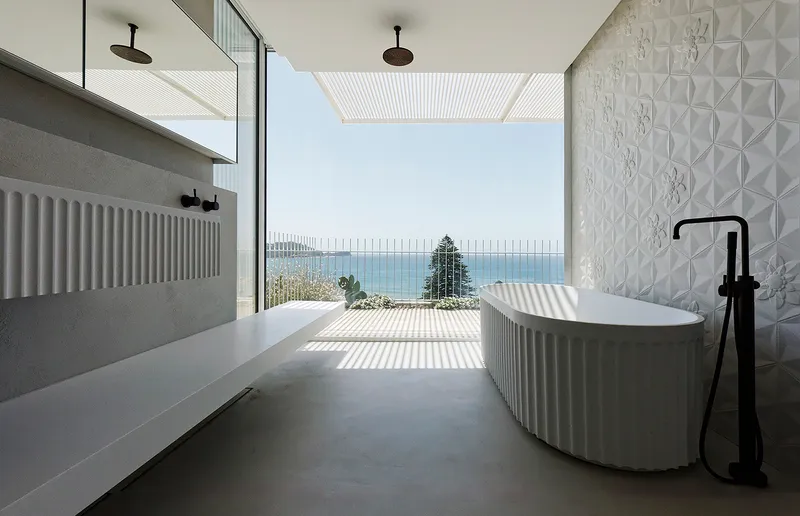 Bathroom with freestanding tub and textured tile wall opening to ocean view through corrugated screen