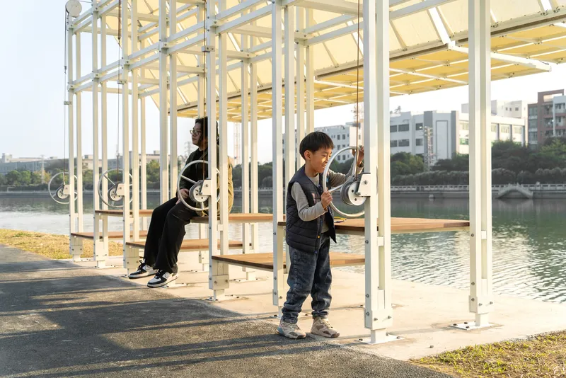 Children playing inside the white steel frame pavilion with river view beyond the columns