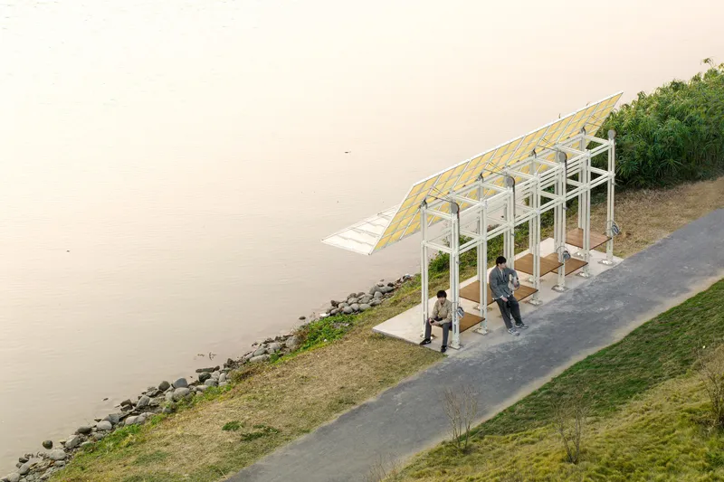 White steel frame shelter with built-in seating benches where two visitors rest by the water