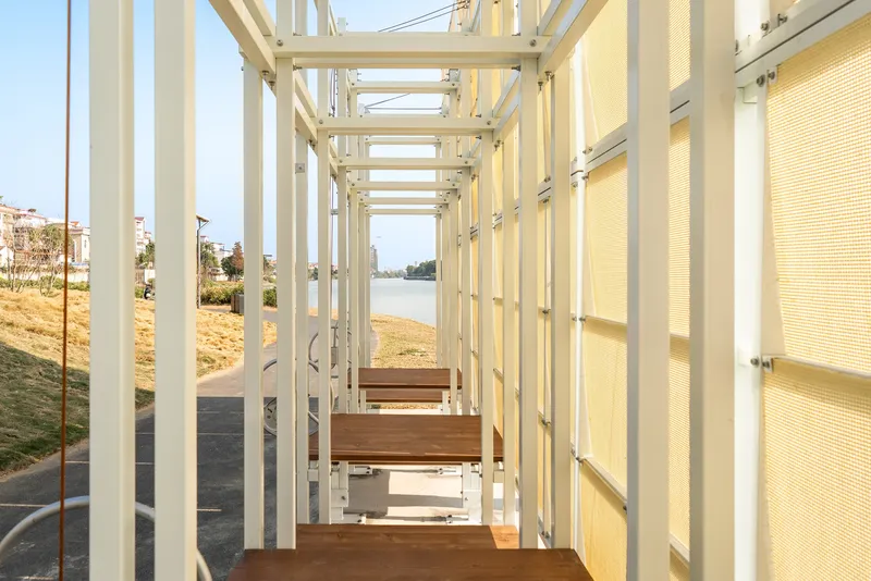 Interior view through white steel columns and timber benches framing the river beyond