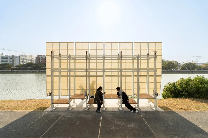 Translucent yellow panel shelter with steel frame and benches beside a river on a clear day