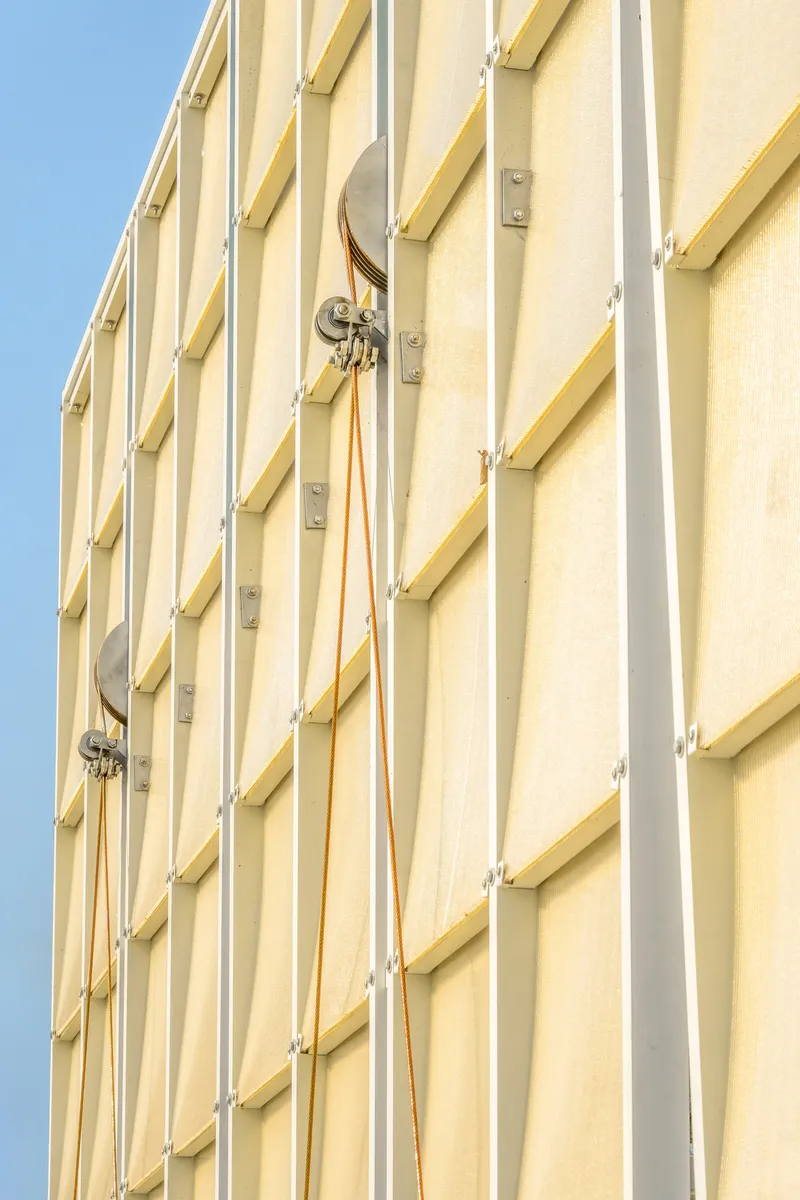 Close-up of the vertical yellow fabric panels with metal clips and cables against blue sky