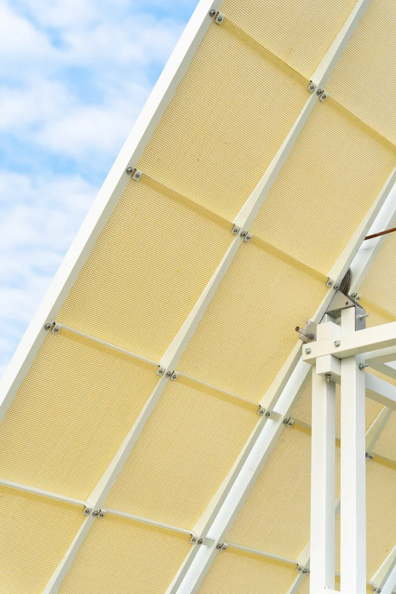 Underside view of the pitched canopy with yellow mesh panels held by white steel joinery