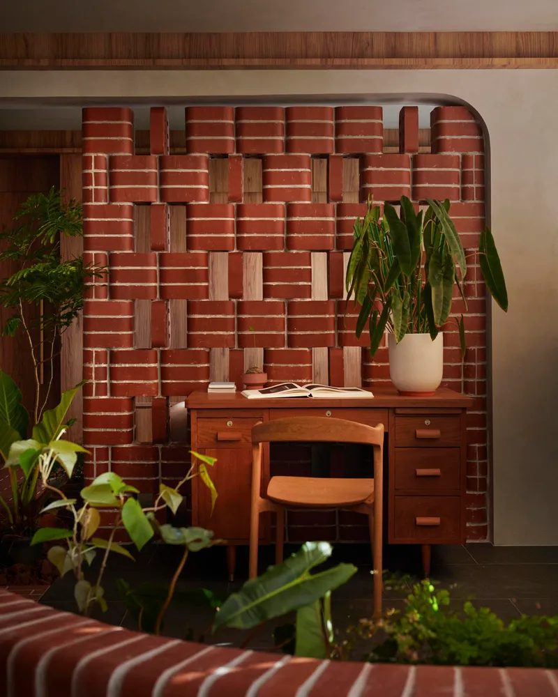 Timber desk tucked into a woven brick and wood niche alcove surrounded by leafy potted plants