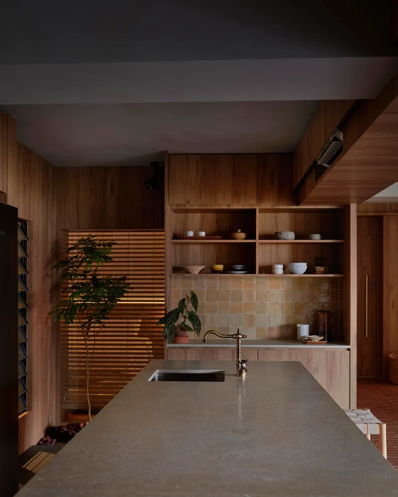 Concrete kitchen counter with horizontal timber louver screen filtering daylight beside open shelving