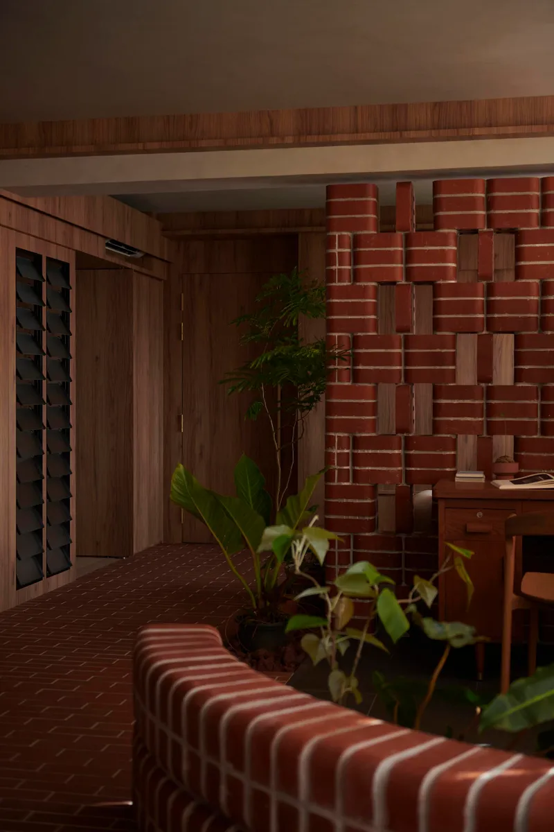 Layered red brick wall forming an undulating relief surface beside planted greenery