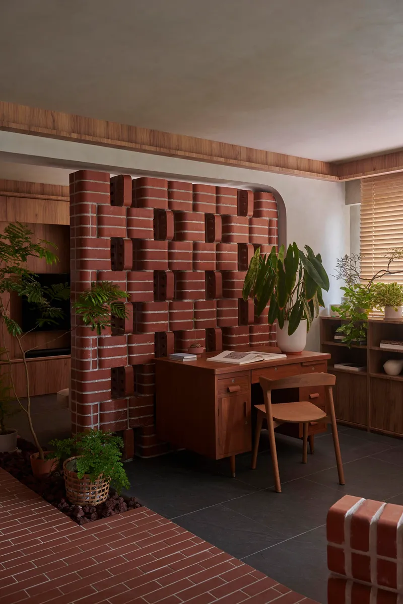 Sculptural red brick wall with protruding blocks behind a timber desk and potted plants