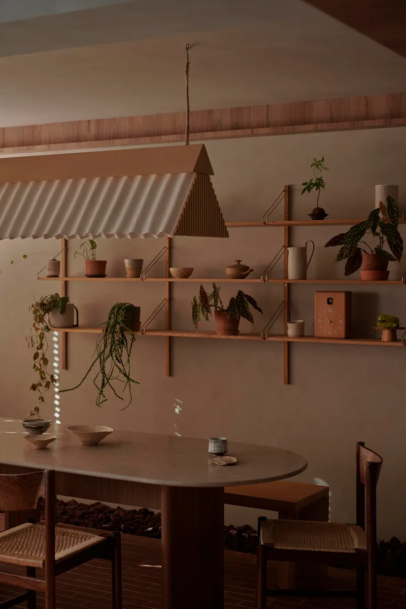 Oval dining table with cane-seated chairs beneath timber shelves and corrugated pendant shade