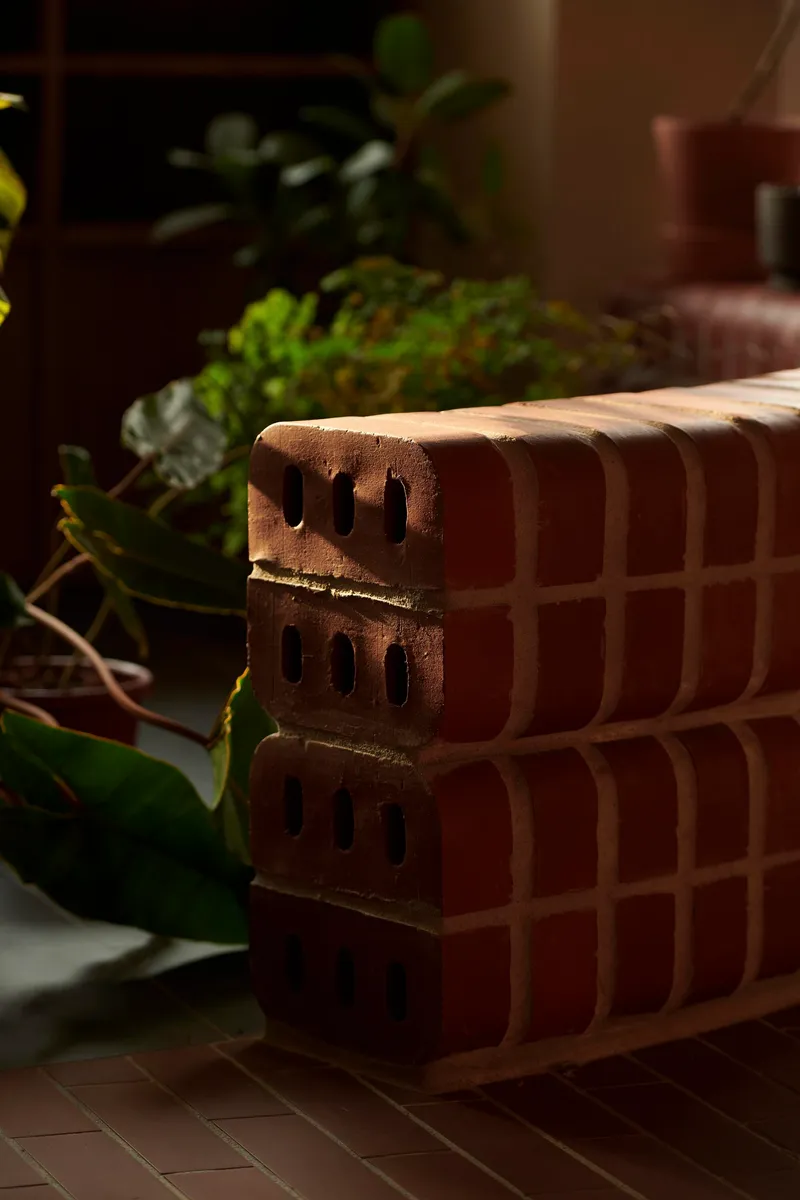 Close-up of terracotta brick stack with perforations beside potted greenery in dappled sunlight