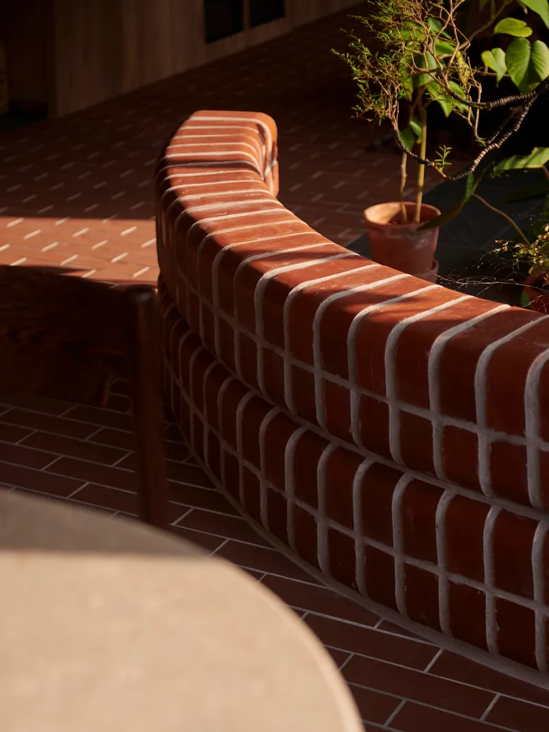 Curved terracotta brick planter wall with shadow patterns cast by overhead slats and potted tree