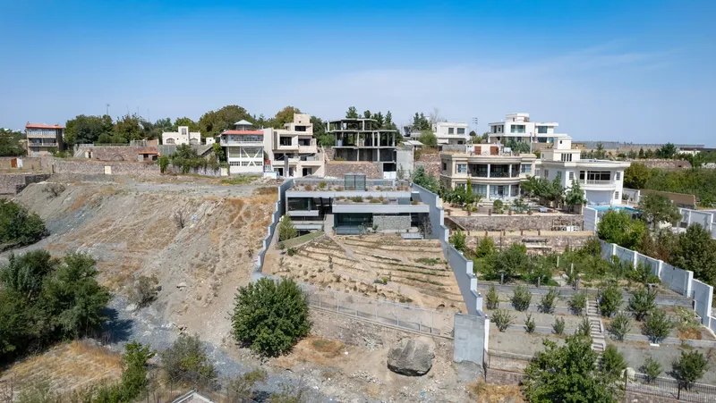 Drone view of the flat roofed volumes stepping down the slope with newly planted terraces below