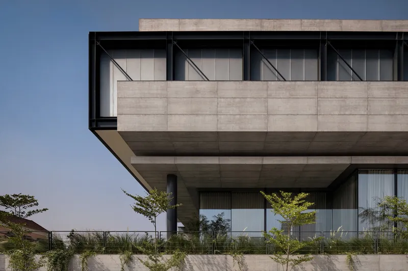 Cantilevered concrete slab soffit above glazed facade and planted terrace with young trees under clear sky