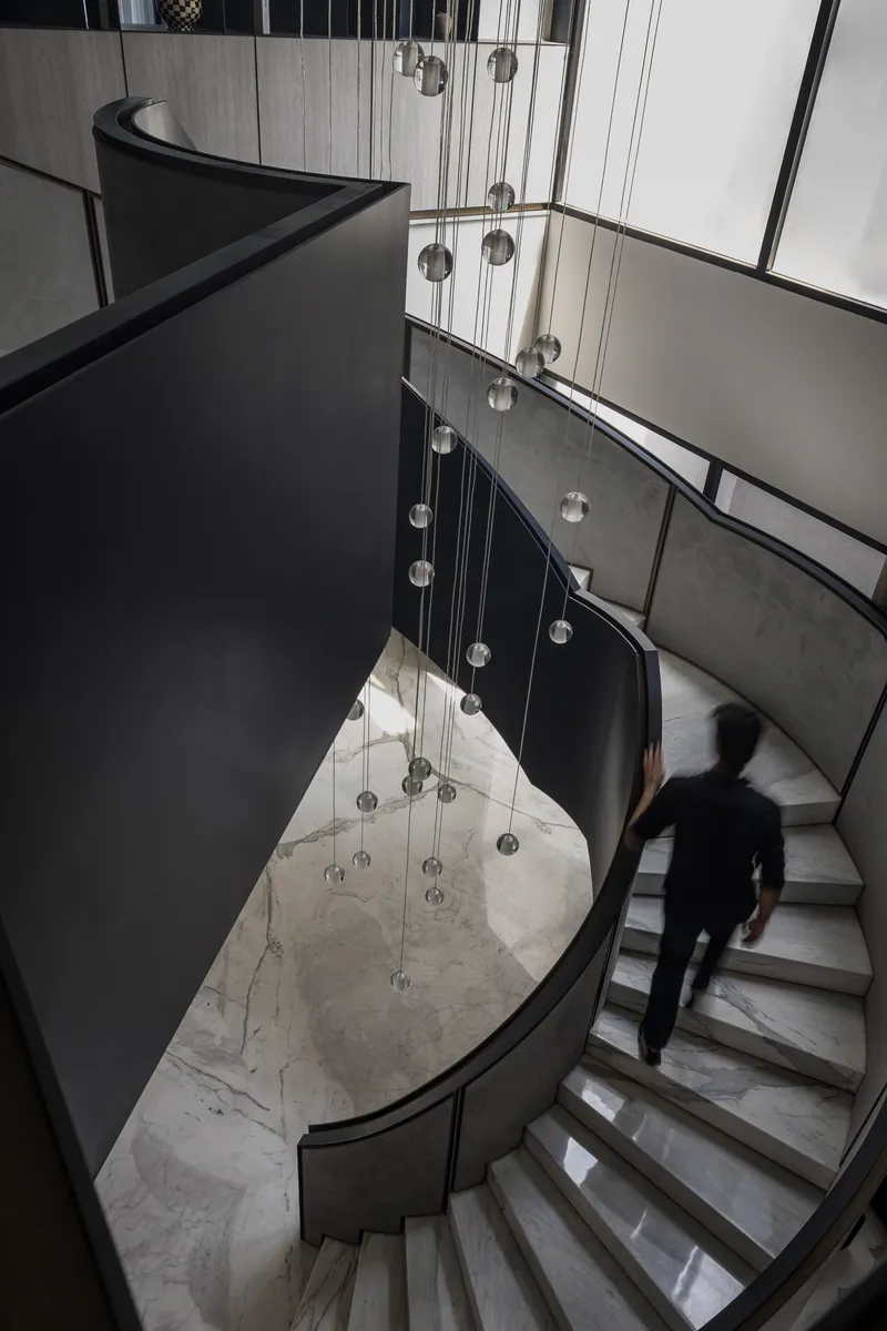 Looking down at curved staircase with marble treads, cluster of globe pendant lights and ascending figure