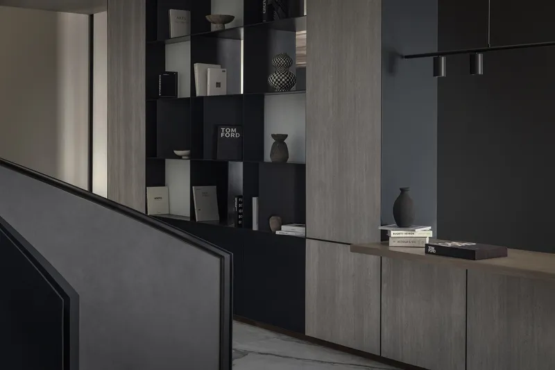 Interior display wall with black recessed shelving holding books and objects beside wood-paneled cabinetry