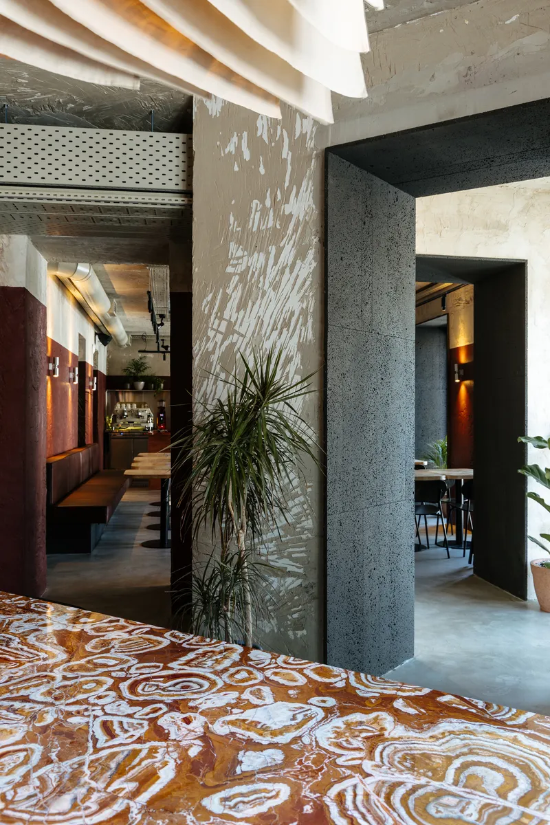 Concrete columns dividing rooms with polished terrazzo floor pattern and potted plants catching dappled light