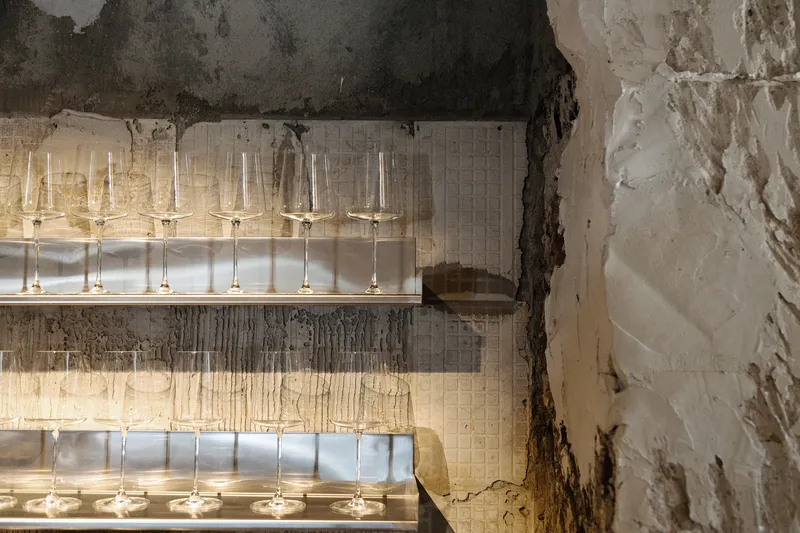 Wine glasses arranged on illuminated shelves against distressed plaster wall revealing layers of old finishes