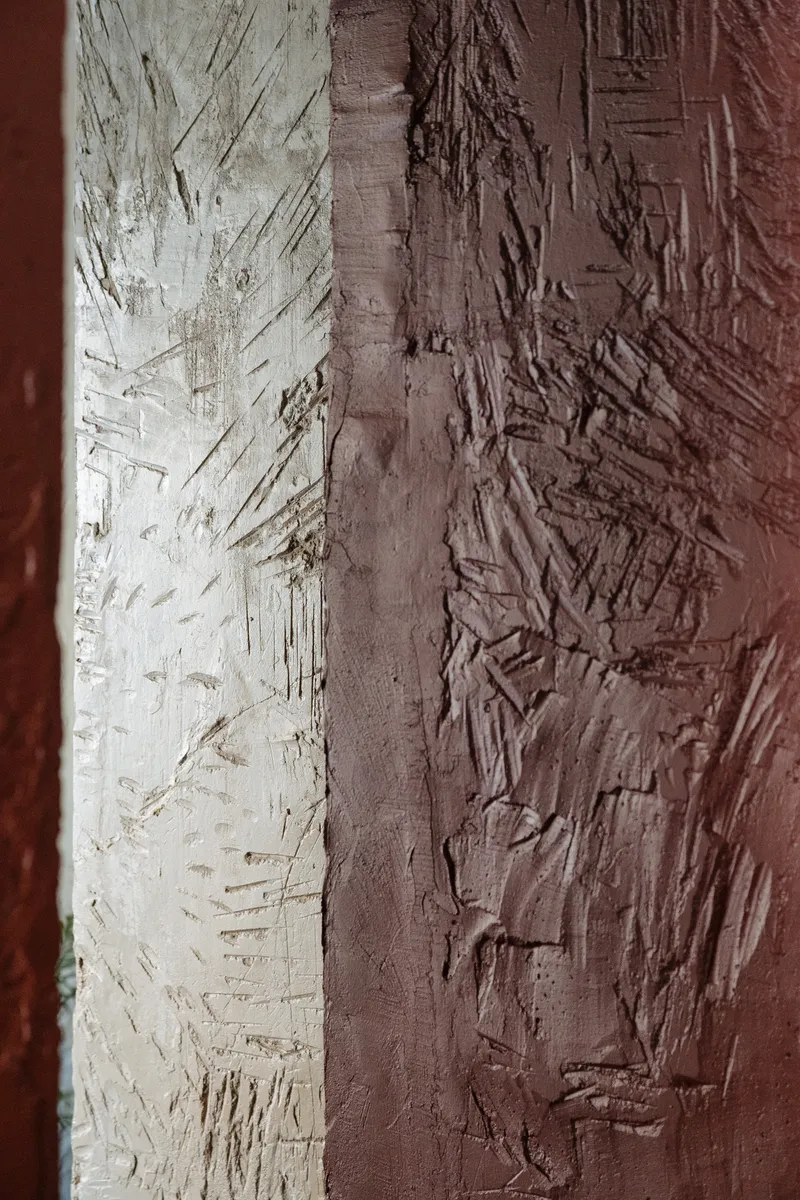 Close-up of textured plaster wall showing transition from white to terracotta with trowel marks