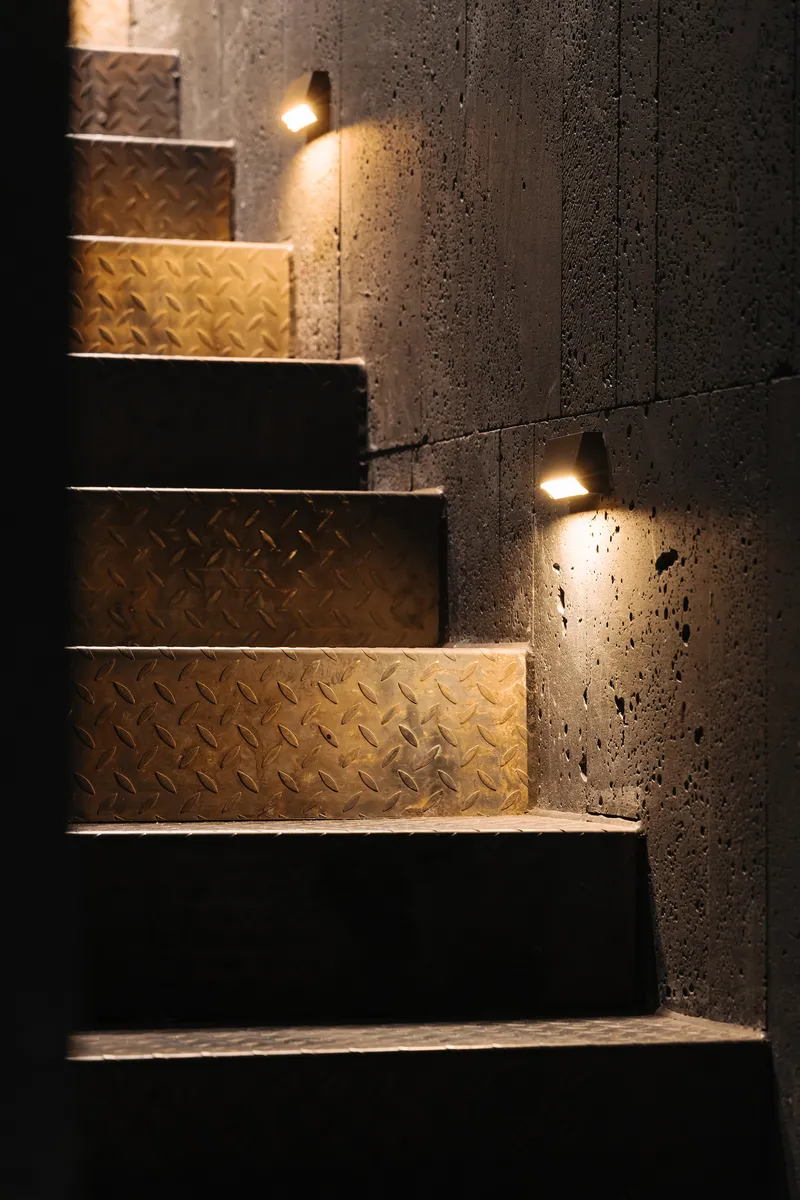 Staircase with diamond-plate metal treads and concrete walls fitted with recessed lighting at night