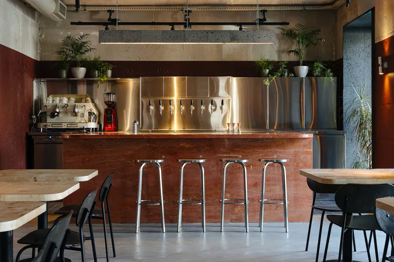 Frontal view of the bar with stainless steel backsplash, tap handles and espresso machine under track lighting