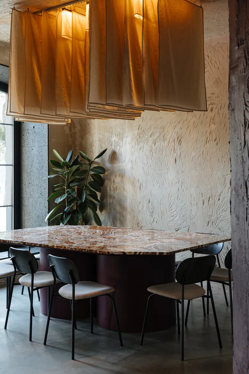 Dining table with marbled top and fabric pendant lamp against textured plaster walls