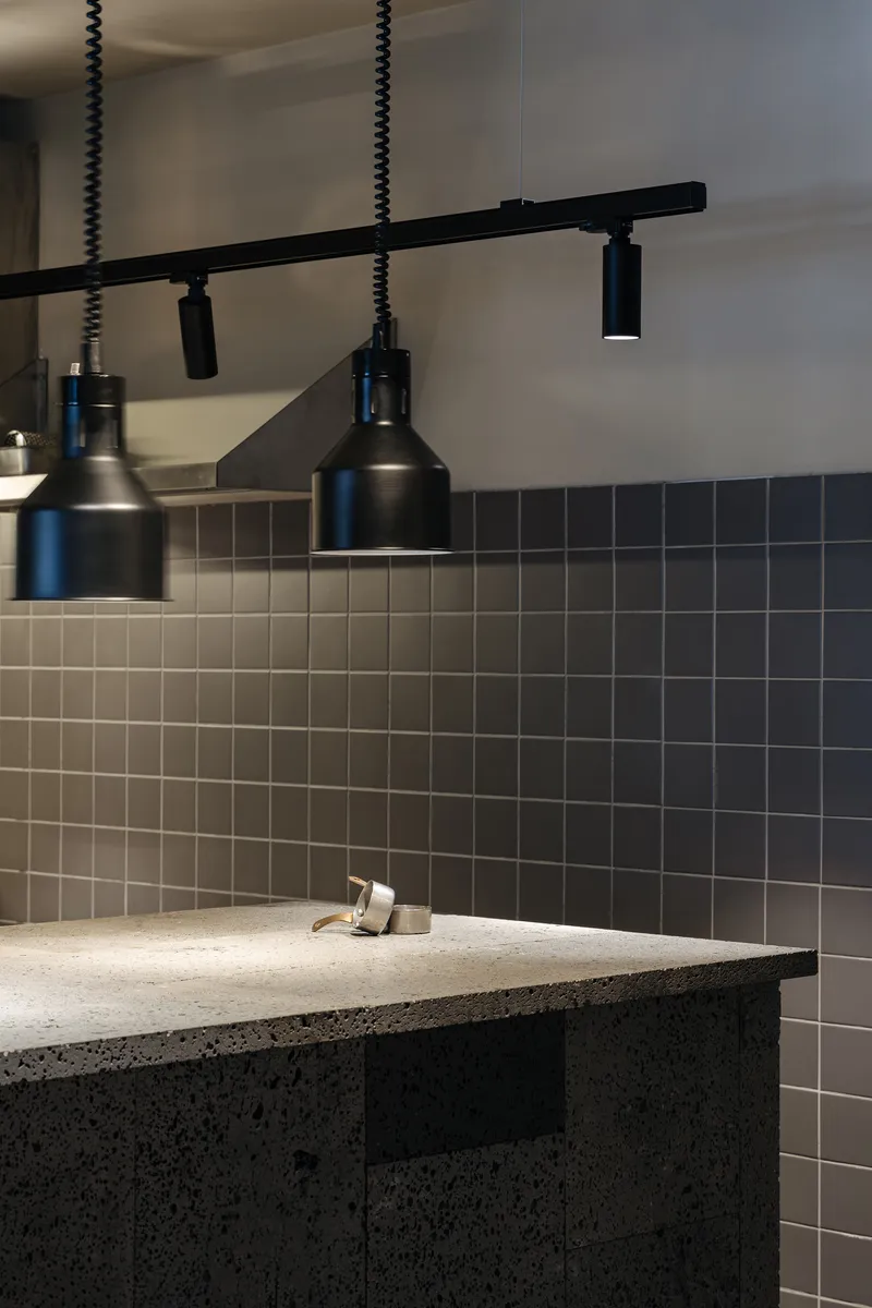 Bathroom sink with dark mosaic tile backsplash and black pendant track lighting above