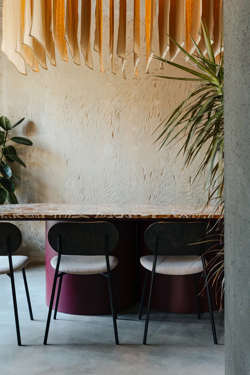 Dining area with textured white wall, slatted timber ceiling feature, and potted plants framing the table