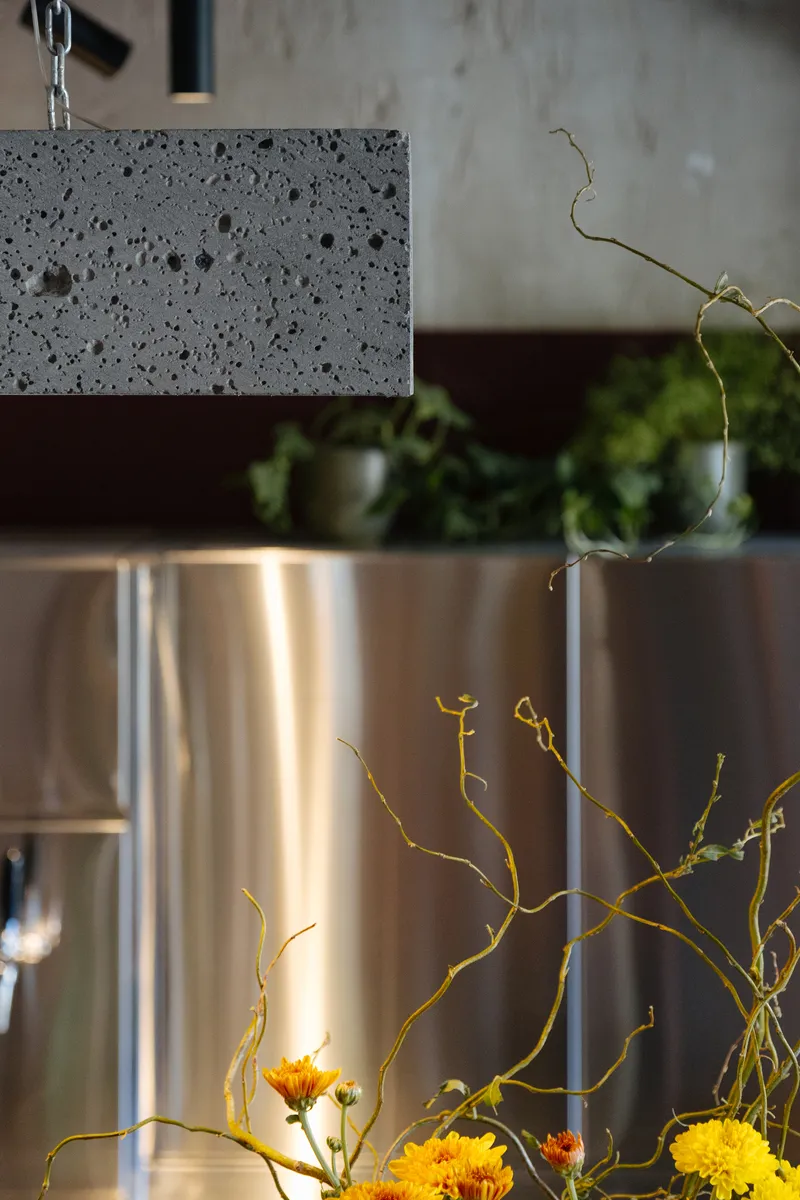 Chain-hung concrete pendant above a vase with yellow flowers and bare branches on polished counter
