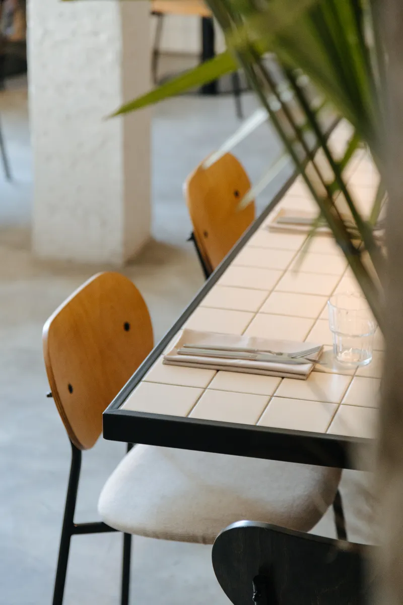Tiled bench seating with rounded plywood backrests beside cream tile tabletop and palm frond shadow
