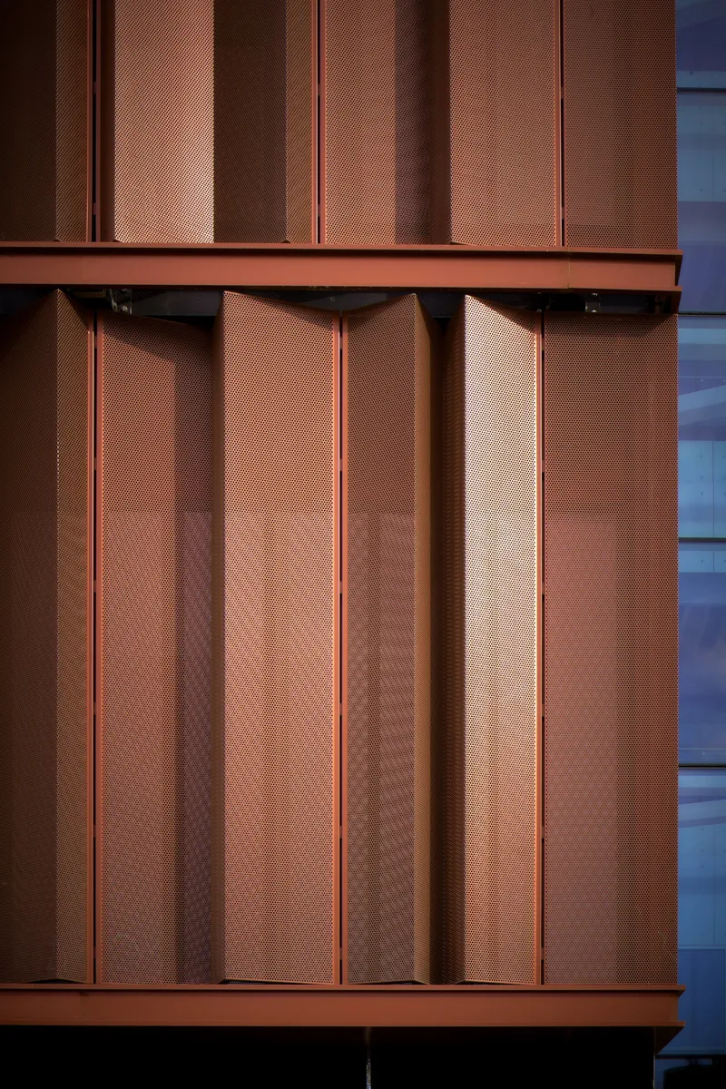 Detail of the perforated copper facade panels framed by horizontal bands at dusk