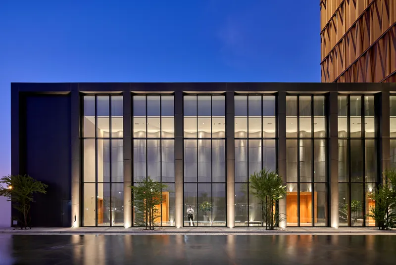 Glazed entrance facade with tall curtain wall and reflecting pool at dusk with a figure inside