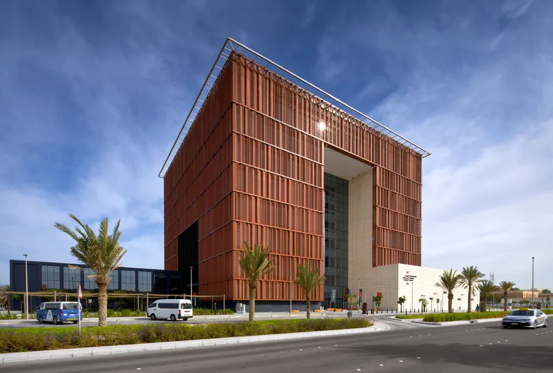 Cube-shaped volume clad in copper vertical louvers at a landscaped roundabout with palm trees