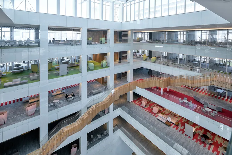 Multi-story atrium with open floor plates, tiered seating areas, and daylight from overhead glazing