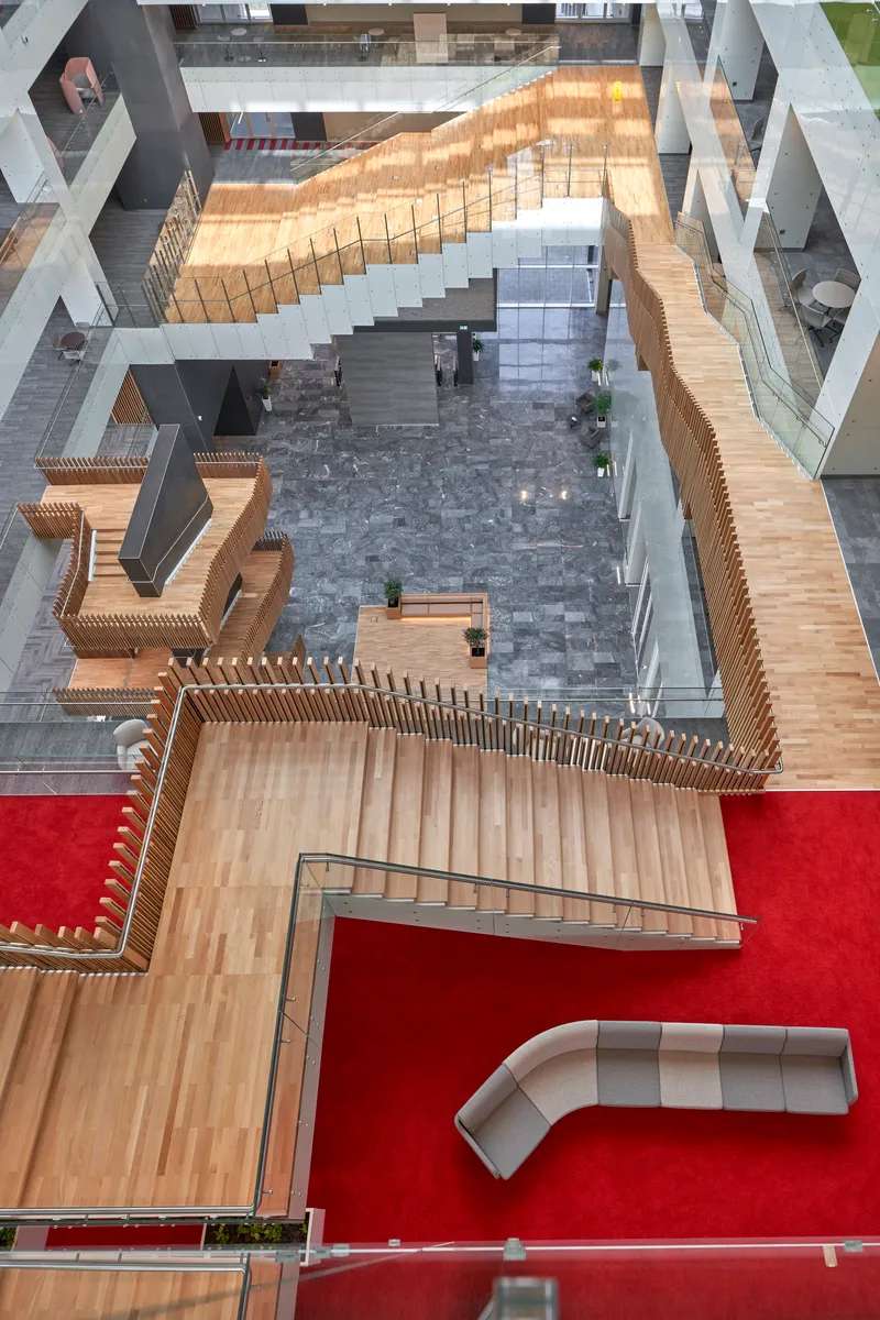 Top-down view of the atrium showing timber slatted balustrades wrapping stair flights and red carpet zones