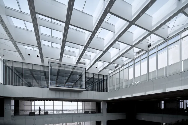 Interior courtyard beneath structural grid skylight with person walking along upper-level bridge