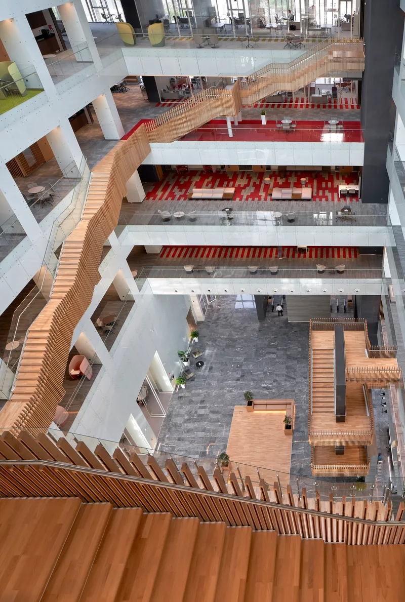 Looking down into a multi-story atrium with slatted timber staircase wrapping around white volumes