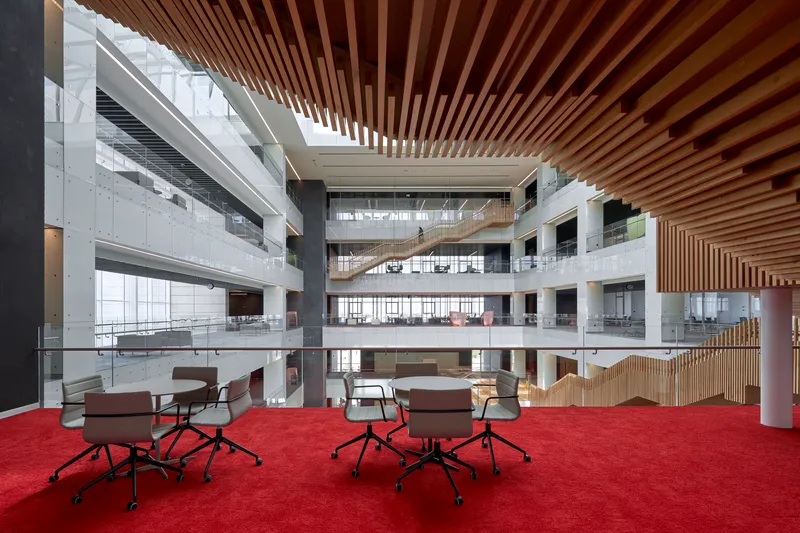 Atrium level with red carpeted floor and slatted timber ceiling above scattered work tables