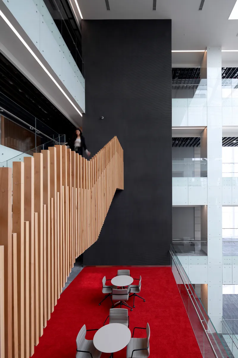 Tall black column beside curving timber-slatted stair balustrade with figure ascending in motion blur