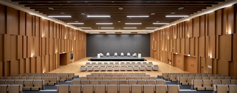 Auditorium with tiered seating facing dark grey stage wall beneath articulated timber side panels