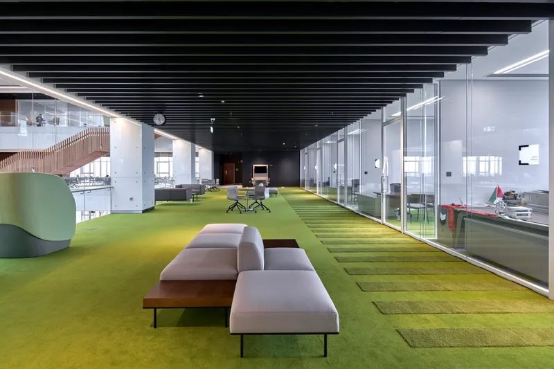 Interior corridor with graduated yellow and green carpet tiles running beneath a black slatted ceiling