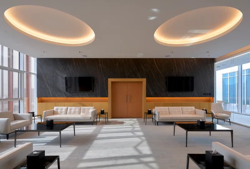 Reception lounge with dark marble wall, paired oval ceiling lights, and sunlight patterning the stone floor