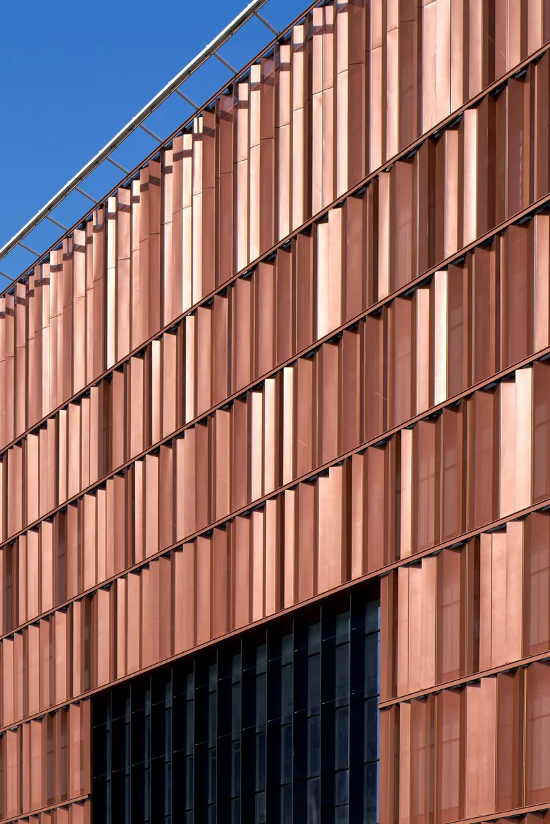 Copper-toned vertical metal cladding on the facade with diagonal shadow lines against a clear blue sky