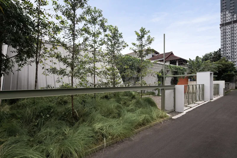 Planted buffer with ornamental grasses and trees along the perforated metal boundary fence beside the road