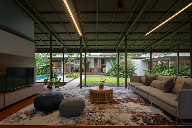 Living room with exposed steel ceiling grid and linear lighting opening to a central courtyard garden