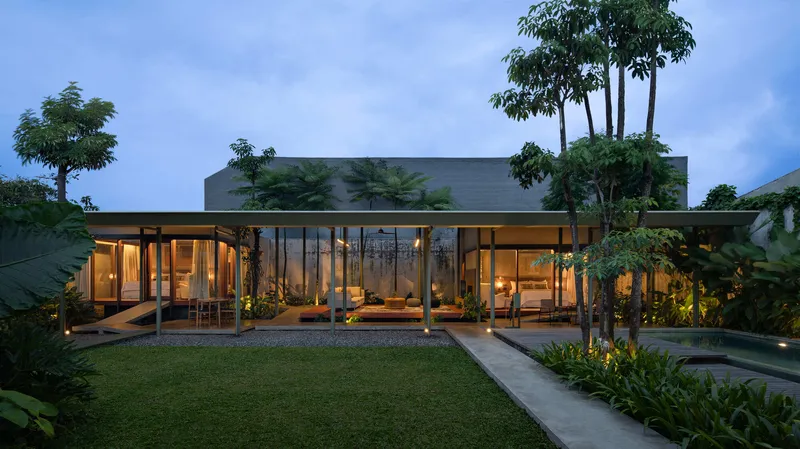 Garden facade of the glazed pavilion with flat roof and interior lighting at dusk