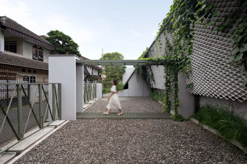 Gravel courtyard with vine-covered perforated facade wall and a figure walking under white plaster volumes