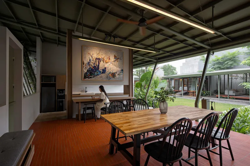 Open dining room with exposed steel structural grid and canted glazing framing a lawn and courtyard