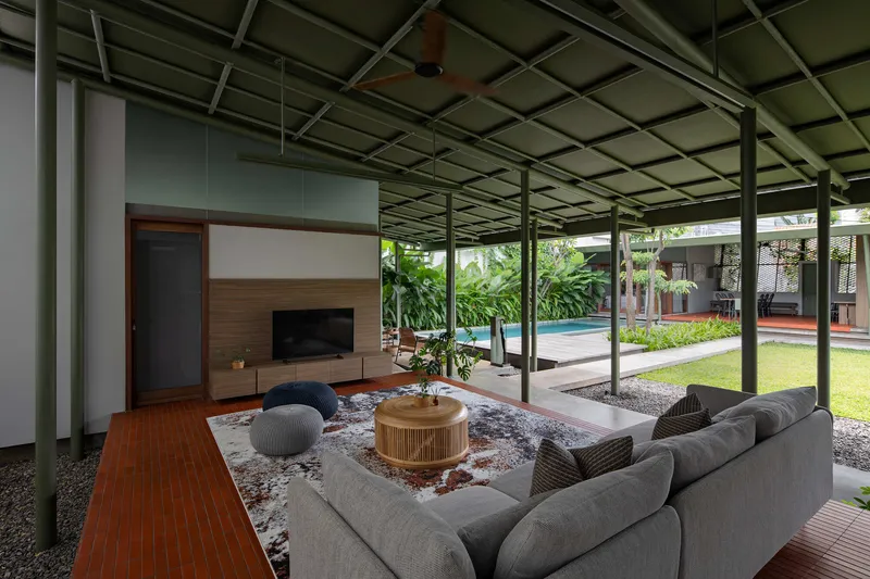 Living area beneath an exposed steel frame ceiling opening to a central lawn and swimming pool