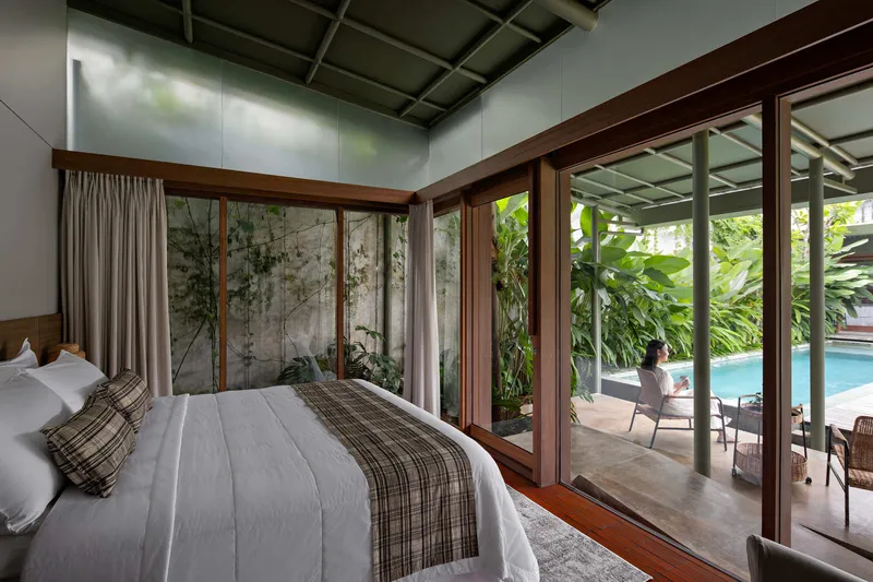 Bedroom with timber-framed glazing looking onto a planted courtyard and pool deck beyond